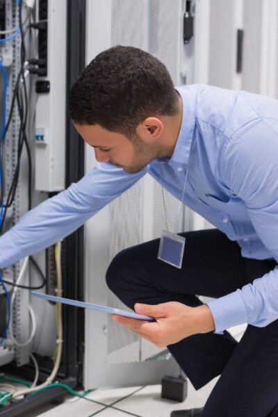 Man checking tablet pc as he is plugging cables into server in data center